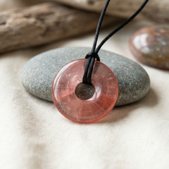 Cherry stone pendant on a black cord with pebbles in the background