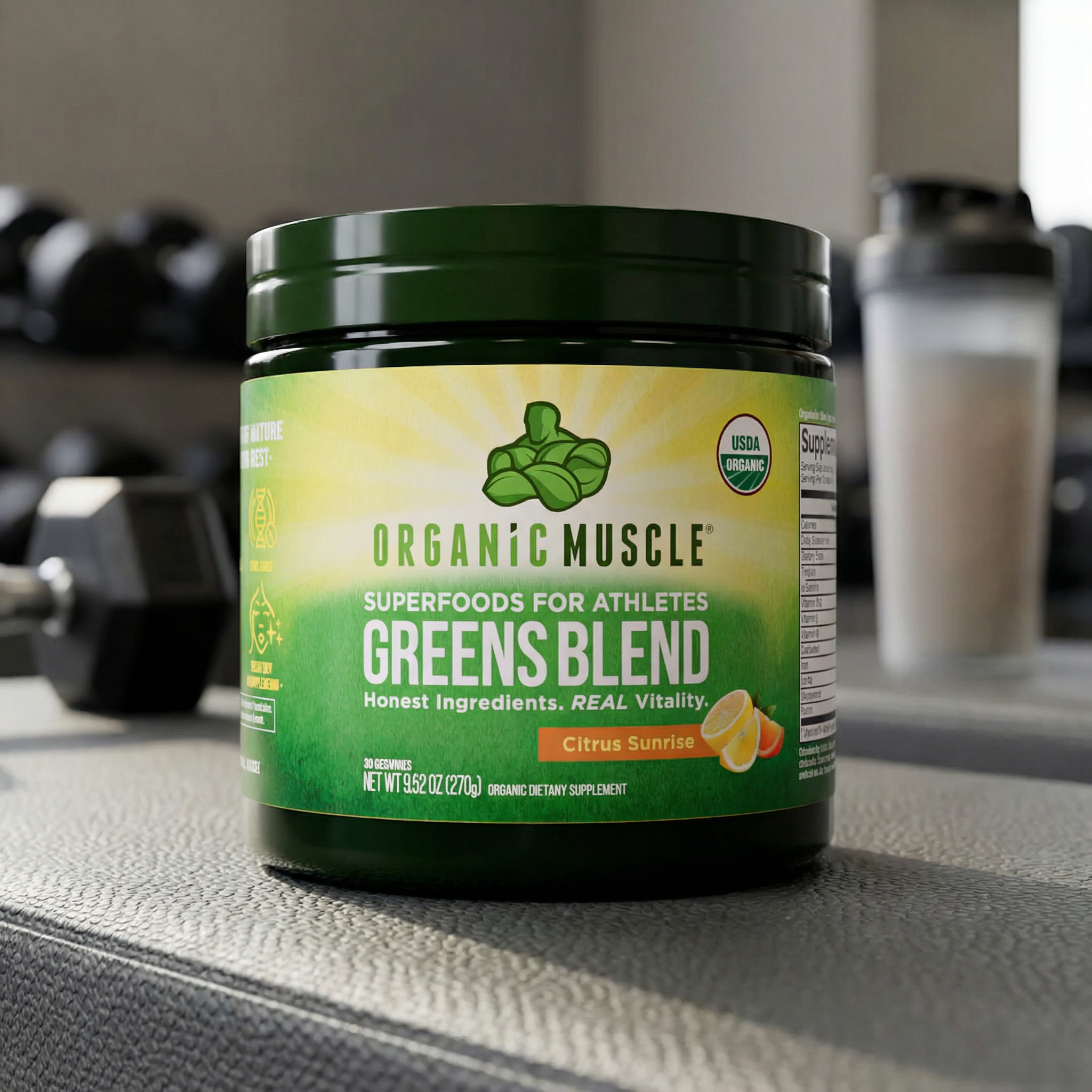 Container of Organic Muscle Greens Blend on a gym counter with dumbbells and a shaker in the background.